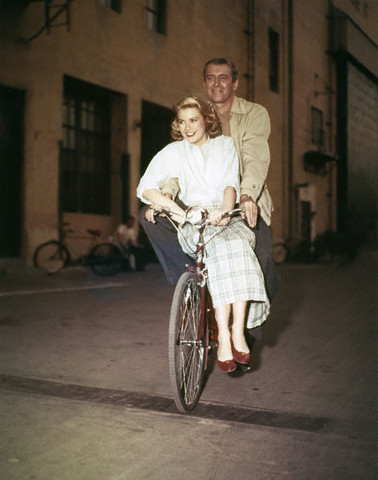 Grace Kelly and Jimmy Stewart ride a bike.